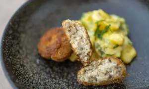 Zwei goldbraune Fischbuletten, eine aufgeschnitten, daneben Kartoffelsalat. Ein leckeres Fischbuletten Rezept.