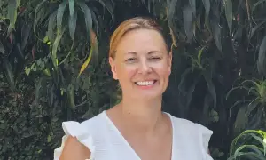 Vrolijke vrouw met blonde haren, lachend in een witte jurk, tegen een achtergrond van weelderig groen. Arjan van Dam zou trots zijn op deze foto.