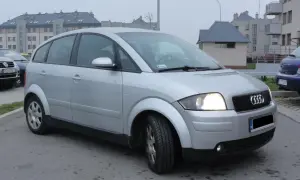 Srebrne Audi A2 zaparkowane przed blokami mieszkalnymi.