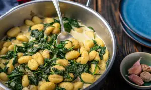 Gnocchi ze szpinakiem w kremowym sosie, podane w metalowej patelni, obok czosnku i gałki muszkatołowej.
