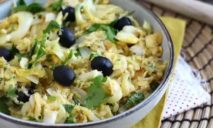 Un plat de bacalhau à bras, mélange savoureux de morue effilochée, d'oignons, d'œufs brouillés et d'olives noires, garni de persil frais.