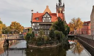 Gdańsk ciekawostki: malowniczy dom z muru pruskiego nad kanałem, w tle wieża kościelna i jesienne drzewa.