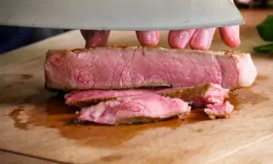 Ein saftiges Kalbskotelett sous vide wird auf einem Holzbrett in Scheiben geschnitten.
