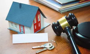 Modellino di casa, chiavi e martelletto del giudice su un tavolo di legno, simboli della procedura pignoramento immobiliare.