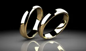 Dos alianzas doradas, una al lado de la otra, reflejándose en una superficie pulida. La diferencia entre alianza y anillo de compromiso se ve en su diseño.