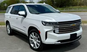 Biały Chevrolet Tahoe z chromowanymi felgami stoi na drodze, otoczony zielenią i chmurami.