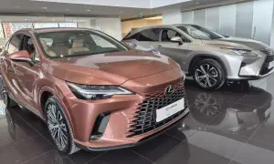 Dwa luksusowe SUV-y Lexus w salonie. Jeden w kolorze miedzianym, drugi srebrny, błyszczą na wypolerowanej podłodze.