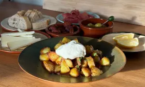 En tallrik med krispiga patatas bravas toppad med en klick krämig sås, omgiven av bröd, ost, chorizo, oliver och citronklyftor.