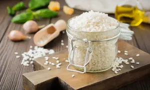 Słoik pełen ryżu **arborio**, idealnego do kremowego risotto. Obok czosnek, bazylia i oliwa.