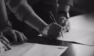 Dłonie podpisujące dokumenty, zbliżenie, czarno-białe.