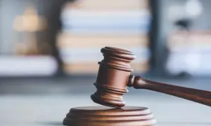 Drewniany młotek sędziowski, symbol sprawiedliwości i pracy asesora sądowego, na tle stosu ksiąg prawnych.