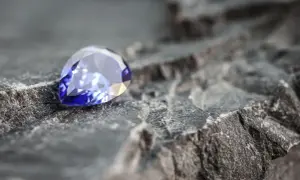 Błyszczący, fasetowany niebieski kamień szlachetny leżący na szarej, chropowatej skale.