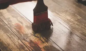 Brocha aplicando una capa de imprimación sobre tablones de madera rústica, preparándolos para un nuevo acabado.