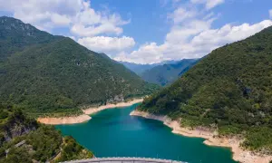 Imponente diga sul lago di Valvestino, circondato da montagne verdi e un cielo azzurro con nuvole bianche.