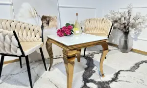 Elegancki stolik do salonu ze złotymi nogami, szklanym blatem, obok krzeseł i wazonu z kwiatami.