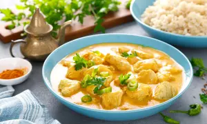 Aksamitny kurczak curry po tajsku w niebieskiej misce, udekorowany kolendrą i papryczką chili. Obok ryż i przyprawy.
