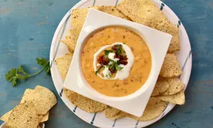 Salsa de queso cremosa en un tazón blanco, rodeada de totopos y adornada con crema y cilantro.