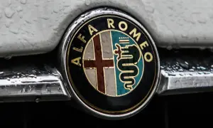 Klasyczne alfa romeo logo z krzyżem i wężem, błyszczące mimo kropel deszczu na karoserii.