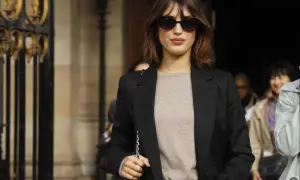 Eine Frau mit braunem Bob und Sonnenbrille trägt typisch französische Kleidung: einen beigen Pullover, Jeans und einen schwarzen Blazer.