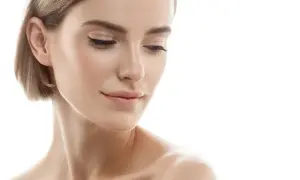 Kobieta z gładką cerą, subtelnym makijażem i krótkimi blond włosami. Jej spojrzenie skierowane w dół sugeruje refleksję nad tym, jak odmłodzić twarz.