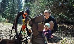 Uśmiechnięta mama przygląda się dziecku w nosidle w górach.