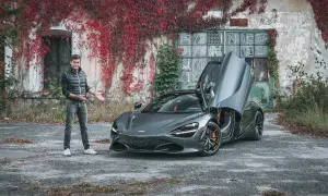 Szary McLaren 720S z otwartymi drzwiami, obok mężczyzny stojącego przy zarośniętym budynku.