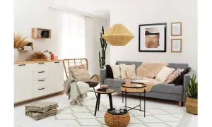 Przytulny salon w stylu rustykalnym z szarą kanapą, wiklinowym fotelem i dekoracjami z naturalnych materiałów.