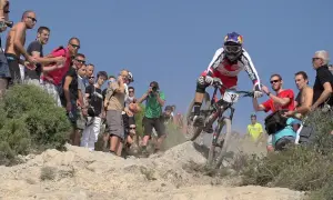 Kolarz w akcji podczas zawodów MTB, otoczony przez widzów i fotografów.