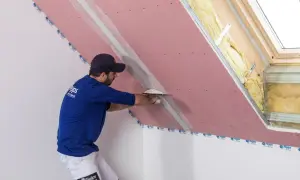 Pracownik wykonuje łączenie płyt gk, nakładając masę szpachlową na taśmę zbrojącą.