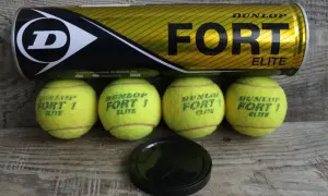 Lattina Dunlop Fort Elite e quattro palline da tennis gialle su fondo in legno. Pronte per una partita!
