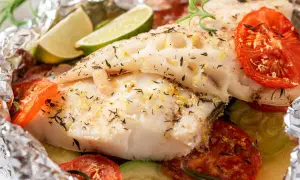 Poisson en papillote savoureux, avec tomates, courgettes, citron vert et romarin, le tout emballé dans du papier aluminium.