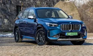 Błękitne BMW iX1 z niebieskimi akcentami stoi na kamienistej nawierzchni przed kamiennym murem.