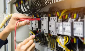 Elektryk sprawdza przewody w szafie sterowniczej. Widać multimetr i liczne kable, w tym przewód neutralny.