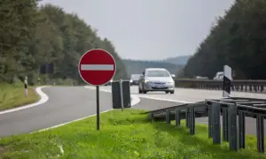Znak b2, zakaz wjazdu, stoi przy krętej drodze. Samochody jadą w tle.