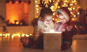 Zwei Kinder mit Rentiergeweih und Weihnachtsmütze öffnen ein leuchtendes Geschenk. Ein magischer Moment im Kindergarten an Weihnachten.