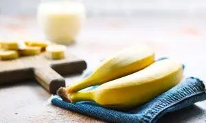 Dwa dojrzałe banany na dżinsowej serwetce, obok pokrojonych bananów i szklanki napoju. Interesuje Cię indeks glikemiczny bananów?