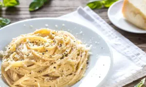 Pyszny makaron na obiad, posypany parmezanem i świeżo mielonym pieprzem. Obok kawałek sera i listki bazylii.