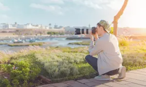 Młody fotograf, ucząc się fotografii dla początkujących, kuca na tle malowniczego portu i miasta, by uchwycić idealny kadr.