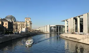 Ein Boot fährt auf der Spree am Reichstagsgebäude und modernen Gebäuden des Regierungsviertels Berlin vorbei.