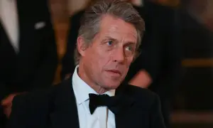 Hugh Grant w czarnym smokingu i muszce, z siwiejącymi włosami, wygląda na zamyślonego.