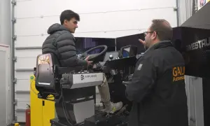 Profesor de autoescuela instruye a un alumno en un simulador de camión. El alumno practica al volante mientras el profesor le da indicaciones.