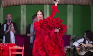Bailaora de flamenco clásico con vestido rojo voluminoso, castañuelas en mano, acompañada por guitarrista y cantaor.