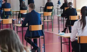Uczniowie siedzą w ławkach na sali gimnastycznej, skupieni na zadaniach. To moment, kiedy sa matury, a przyszłość wielu zależy od tych egzaminów.