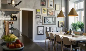 En modern matsal med konst på väggarna, träbord och stolar. En köksdel med fläkt och fruktskål syns till vänster. Massor av matsal inspiration här!