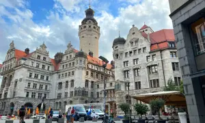 Lipsk trasa: imponujące budynki z wieżą, plac z ludźmi, rowerzystką i kawiarnią pod parasolami.
