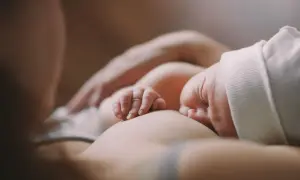 Czułe chwile karmienia piersią. Dziecko ulewa mimo odbicia, ale mama czule je przytula.