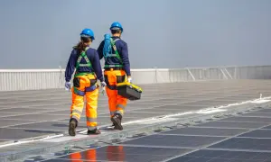 Zwei Techniker in Schutzkleidung gehen über eine Photovoltaikanlage. Regelmäßige Wartung der Photovoltaikanlage ist Pflicht für optimale Leistung.