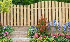 Holz-Gartenzaun-Ideen: Ein schmaler Holzzaun mit Tor, flankiert von bunten Blumen und Ziegelstufen, schafft einen charmanten Eingang.