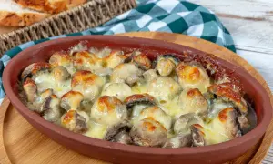 Gorące, zapieczone pieczarki z piekarnika, skąpane w ciągnącym się serze, podane w glinianym naczyniu.