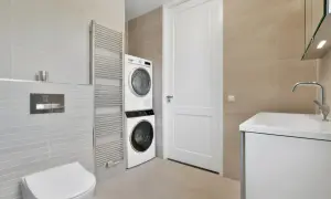 Bagno moderno con doccia e lavatrice vicine. Asciugatrice sopra la lavatrice, vicino a un termosifone cromato e un WC.